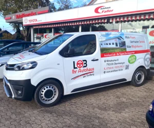 Ein weißer Kastenwagen mit Beschriftung für das Lob Autohaus steht vor dem Schaufenster des Autohauses