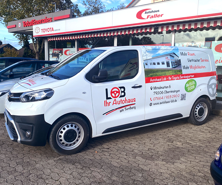 Ein weißer Kastenwagen mit Beschriftung für das Lob Autohaus steht vor dem Schaufenster des Autohauses